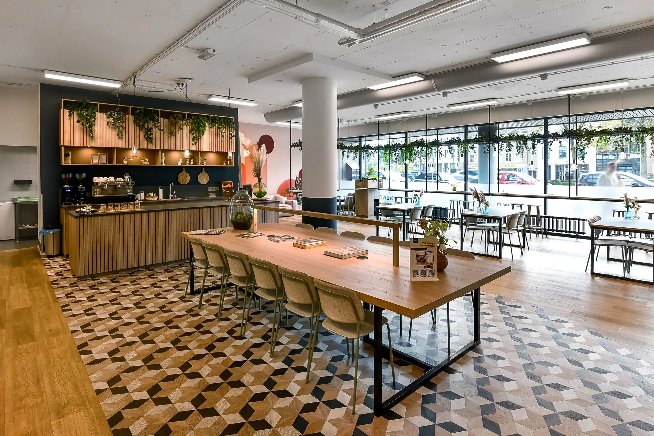 Moderne en sfeervolle ontmoetingsruimte van Newday Arnhem met een koffiebalie, lange houten tafel en grote ramen met uitzicht op de straat.