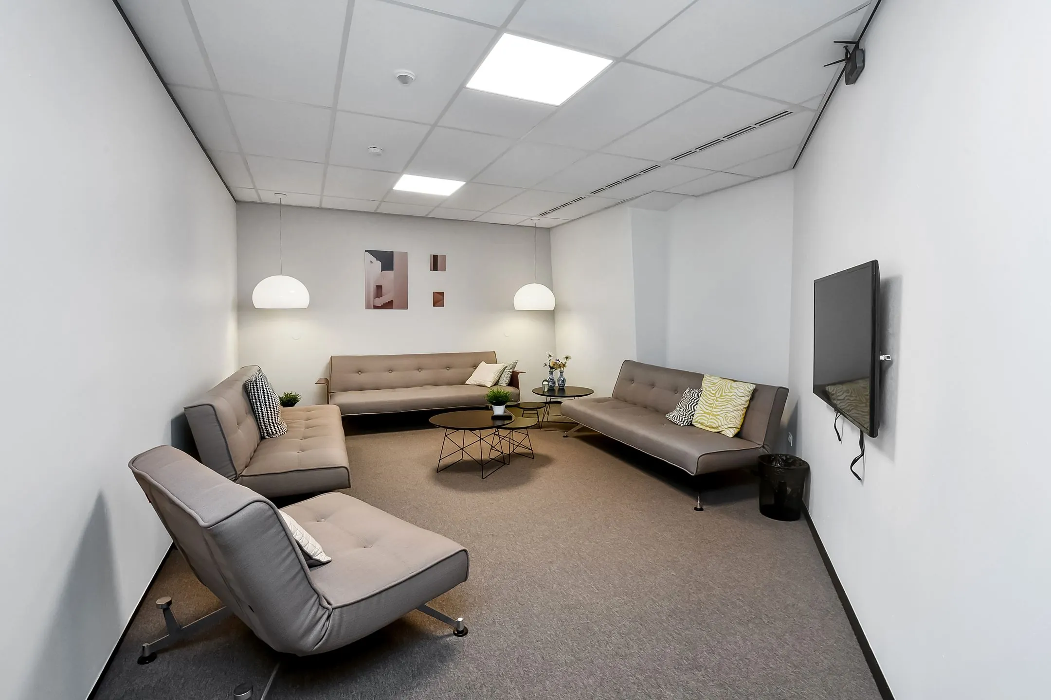 Moderne wachtruimte bij Newday Arnhem met grijze banken, ronde salontafels en een wandtelevisie.