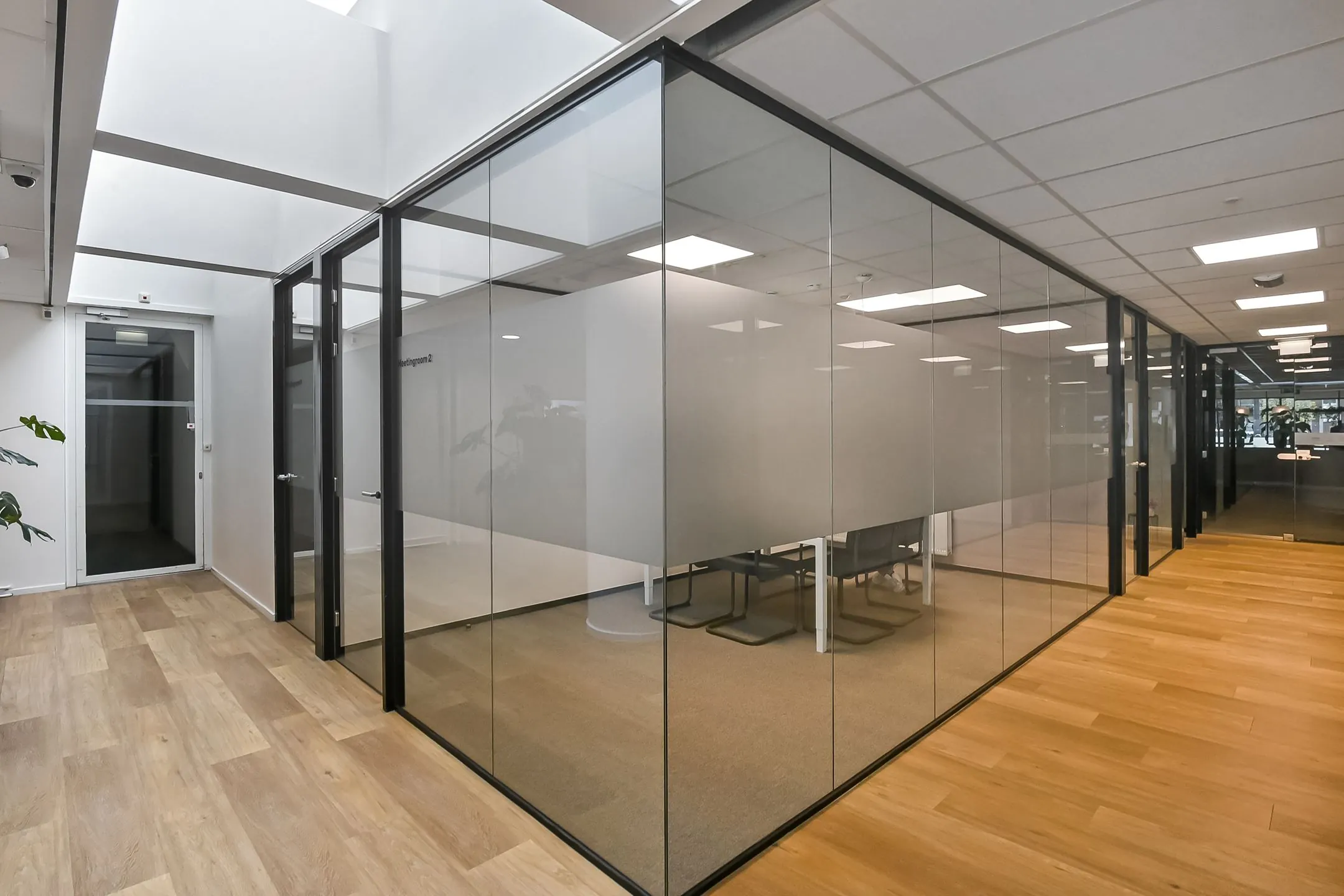 Moderne kantoorruimte bij Newday Arnhem met glazen vergaderruimtes en houten vloer.
