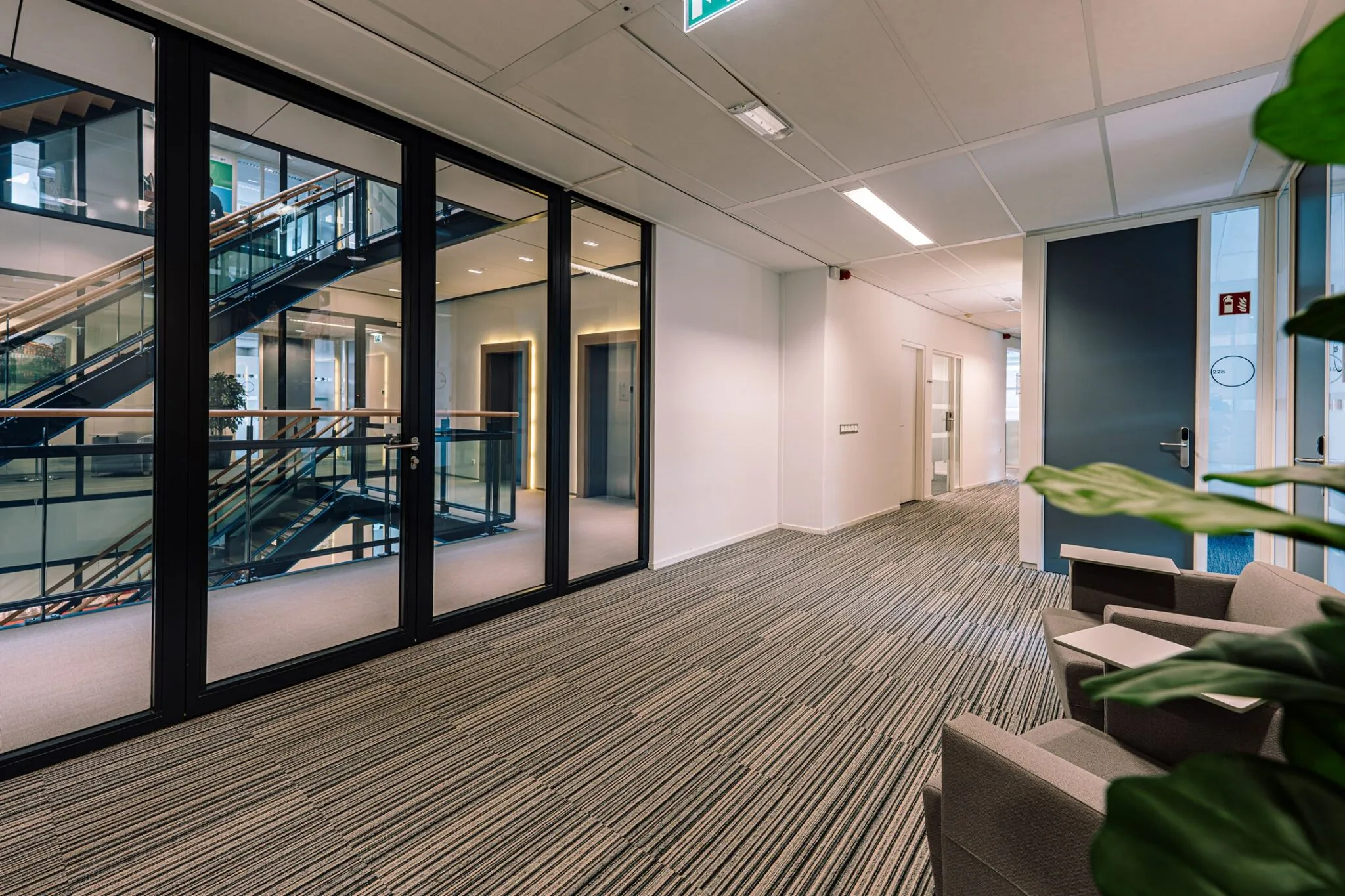 Modern kantoorinterieur aan de Newtonlaan 115 met glazen wanden, zicht op trappenhuis en gestreepte vloerbedekking.