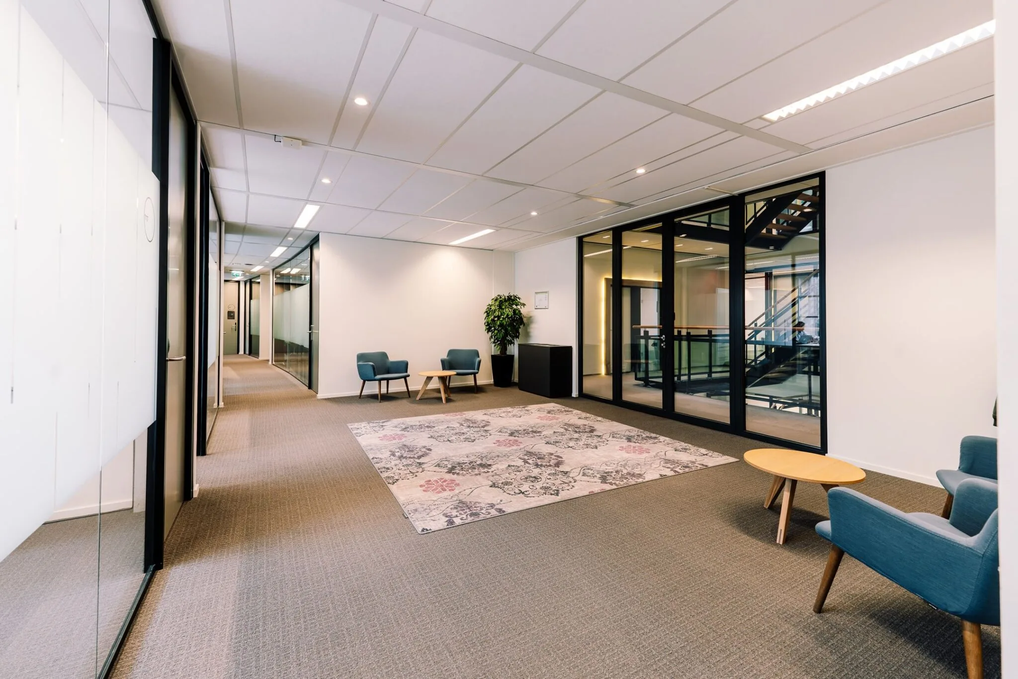 Moderne wachtruimte in een kantoorpand aan de Newtonlaan 115 met blauwe stoelen, een vloerkleed en glazen wanden.