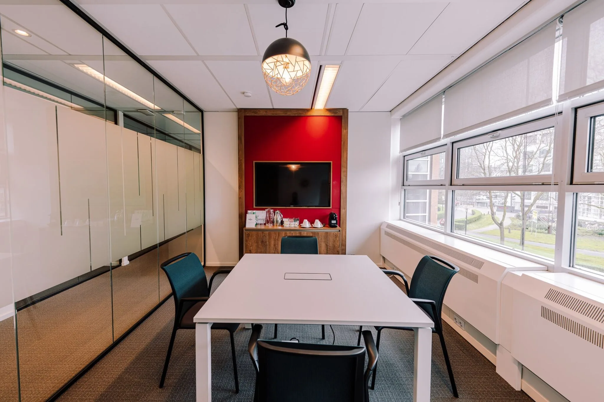 Moderne vergaderruimte aan de Newtonlaan 115 met glazen wand, vier stoelen, flatscreen en koffiecorner.