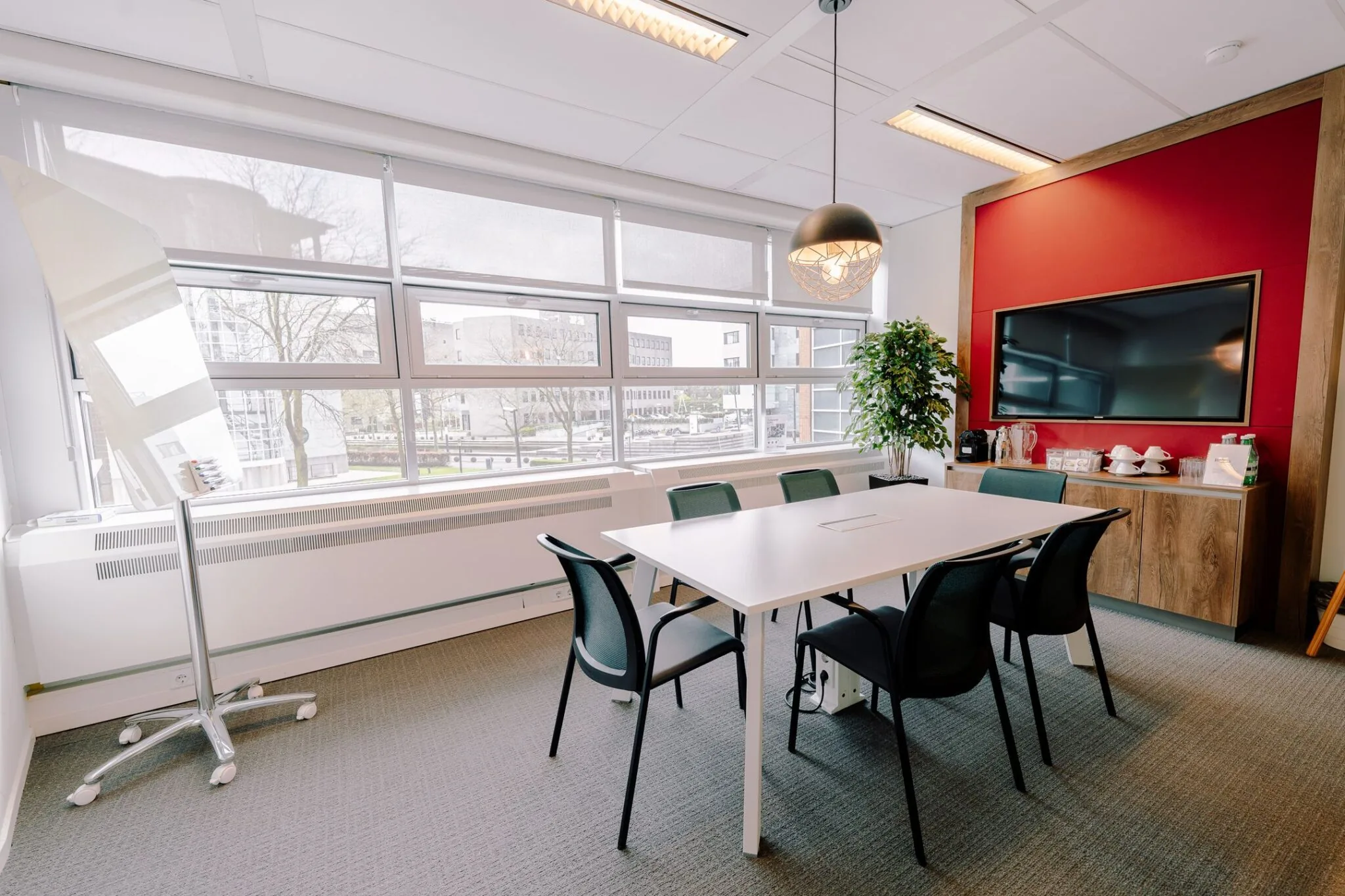 Vergaderruimte met een witte tafel, zes stoelen, groot beeldscherm en koffievoorziening bij Newtonlaan 115.