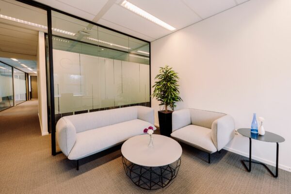 Moderne wachtruimte bij Newtonlaan 115 met twee lichte zitbanken, een ronde salontafel, planten en decoratieve accessoires.