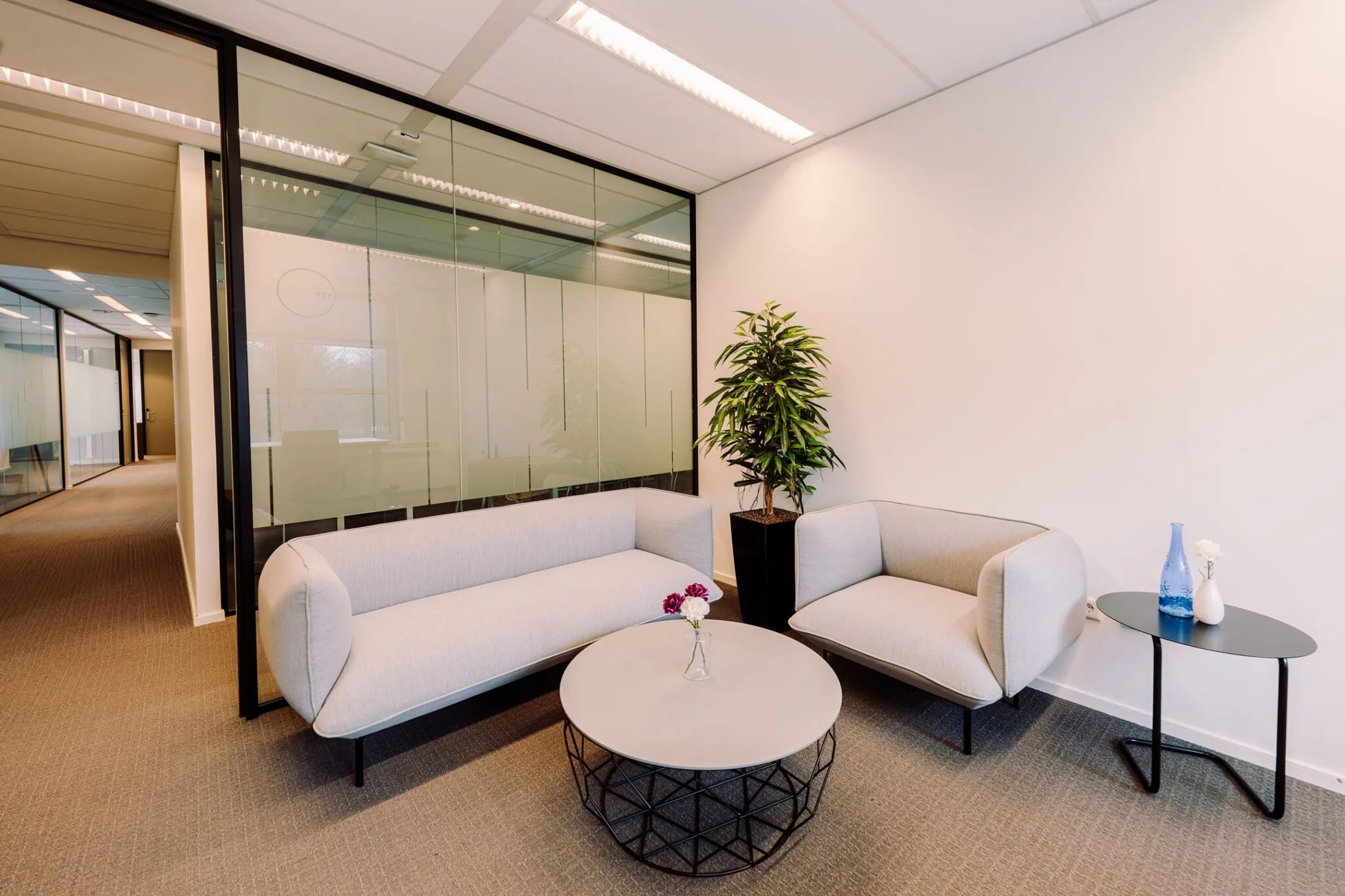 Moderne wachtruimte bij Newtonlaan 115 met twee lichte zitbanken, een ronde salontafel, planten en decoratieve accessoires.