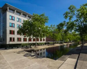 Modern kantoorgebouw aan de Newtonlaan met rode raamkozijnen en een waterpartij omringd door bomen.