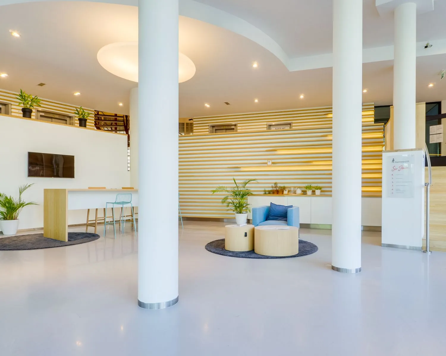 Moderne en lichte ontvangstruimte in het kantoorpand aan de Newtonlaan 51-97, met zitgedeelte, hoge tafel en planten.
