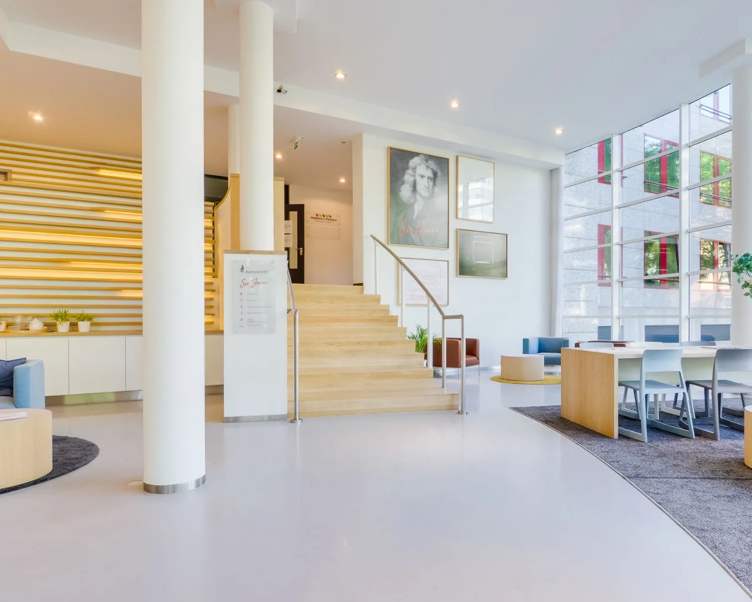 Moderne en lichte entreehal van een kantoorpand aan de Newtonlaan met zitgedeeltes, een trap en grote ramen.