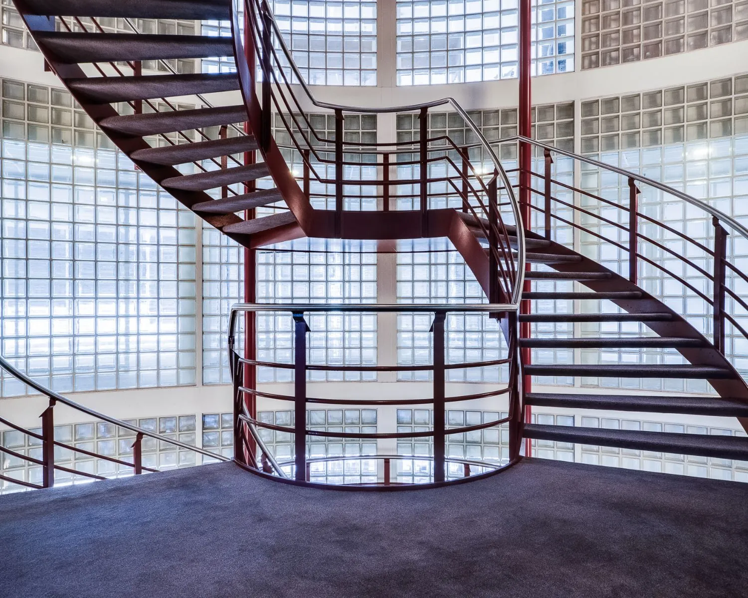 Moderne wenteltrap met rode leuningen in een gebouw aan de Newtonlaan, omgeven door glazen bouwstenen.
