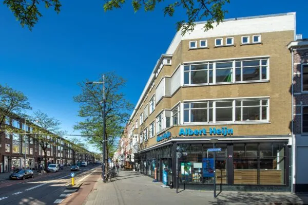 Straatbeeld van de Nieuwe Binnenweg in Rotterdam met een Albert Heijn-winkel op de hoek van het gebouw.