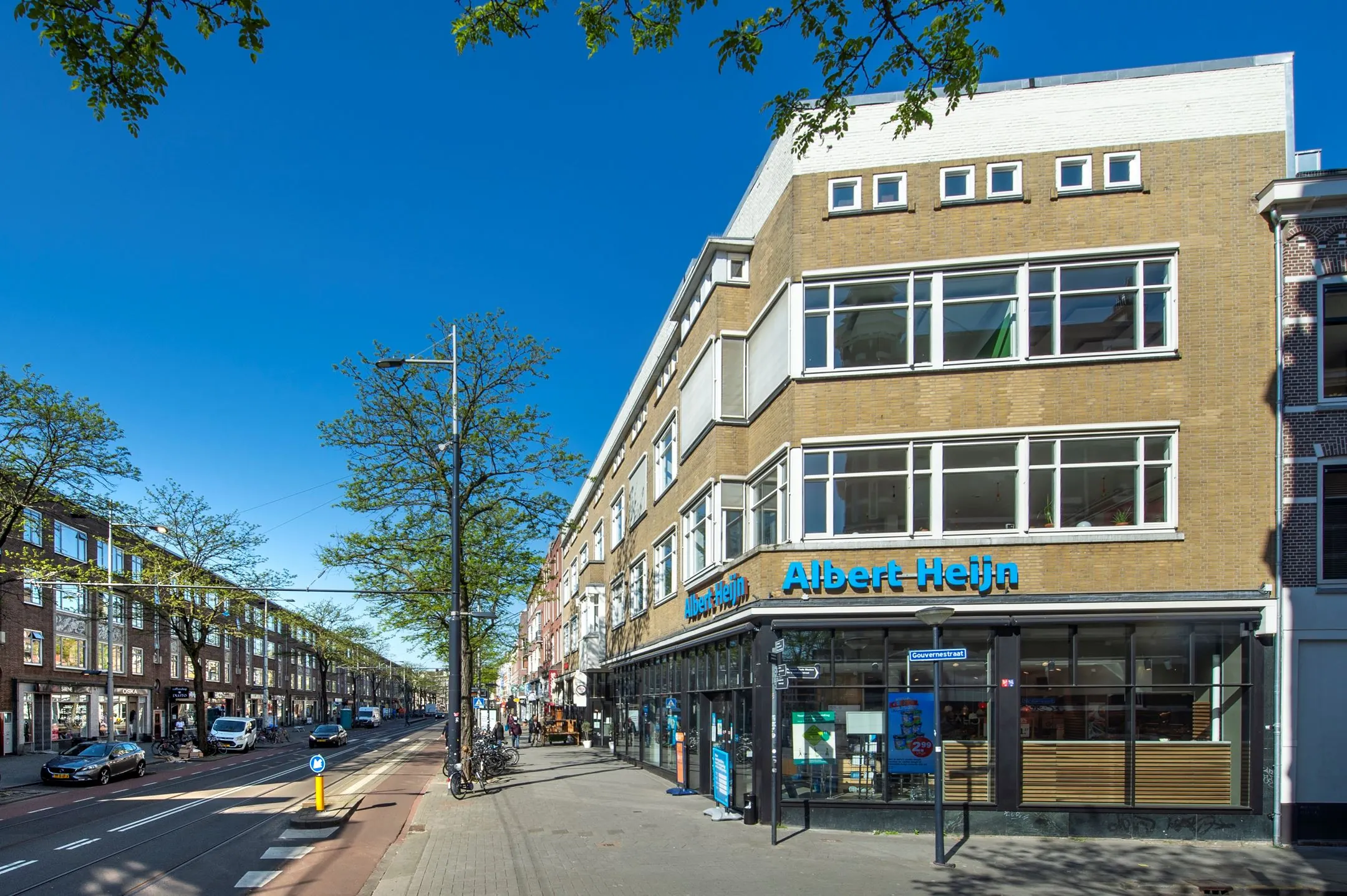 Straatbeeld van de Nieuwe Binnenweg in Rotterdam met een Albert Heijn-winkel op de hoek van het gebouw.