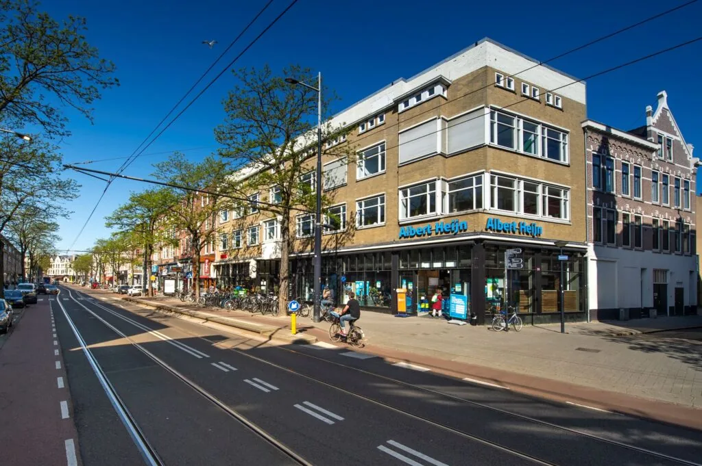 Straatbeeld van de Nieuwe Binnenweg met een Albert Heijn-winkel op de hoek van een bedrijvige straat in Rotterdam.
