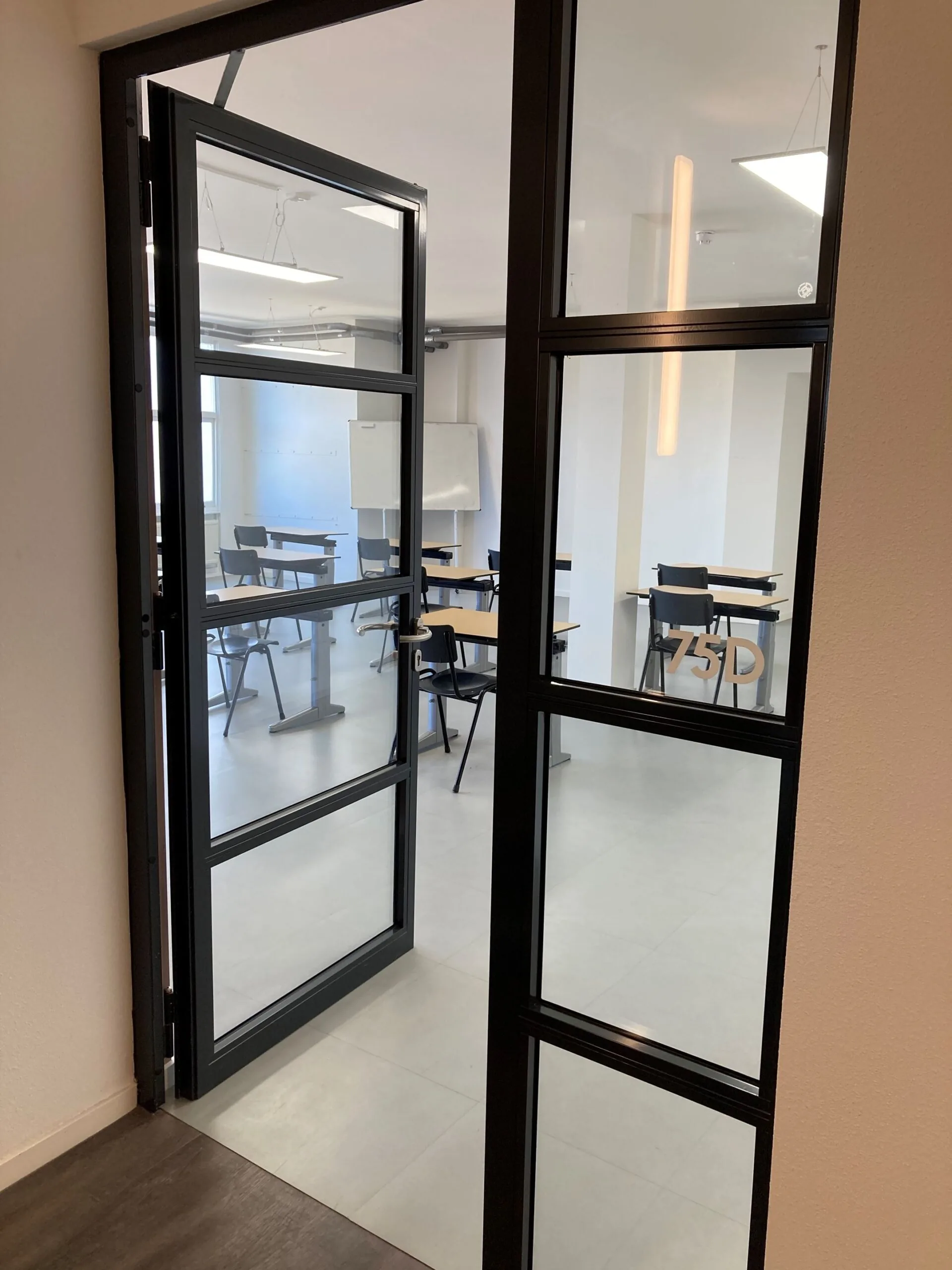 Glazen deur met zwart metalen frame opent naar een modern leslokaal aan de Nieuwe Binnenweg 77E.