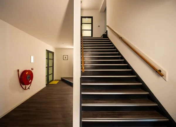 Trap en gang in het interieur van Nieuwe Binnenweg 77 E, met een brandslanghaspel en deur naar unit 25A.