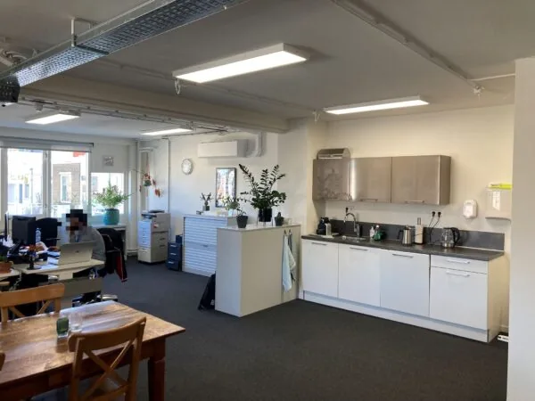 Kantoorruimte aan de Nieuwe Binnenweg 77 E met open keuken, werkplekken en planten bij het raam.