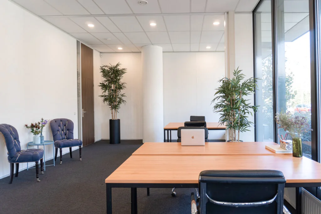 Modern ingerichte kantoorruimte in Office Hotel Fonteinlaan met houten bureaus, zwarte stoelen, planten en grote ramen.