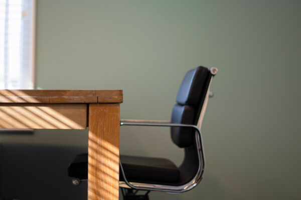 Zwarte bureaustoel en houten tafel in een zonnige ruimte van Office-Hotel Kennemerplein, april 2021.