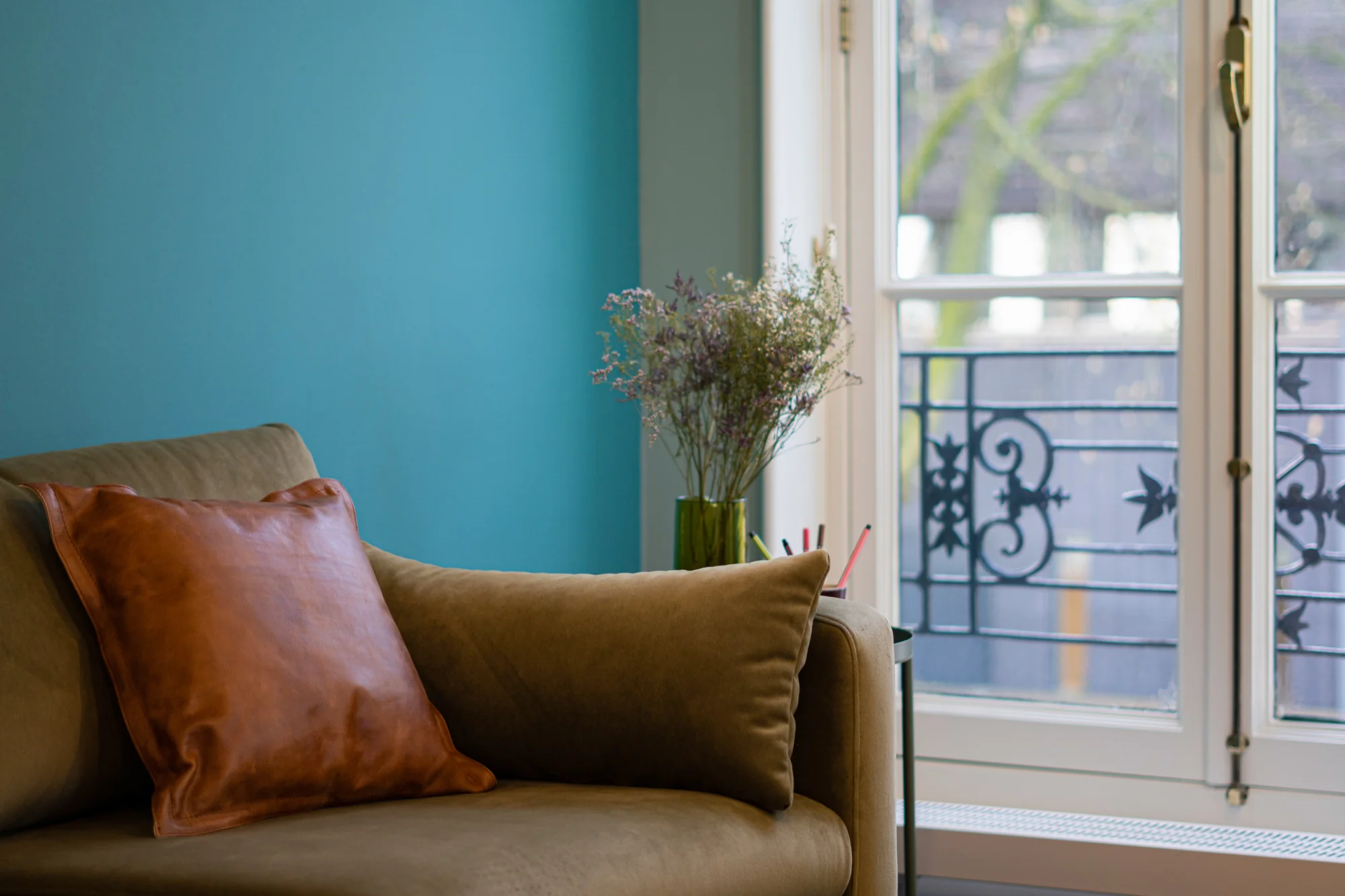 Comfortabele zithoek met een beige fauteuil, leren kussen en vaas met bloemen bij een raam in Office Hotel Kennemerplein.