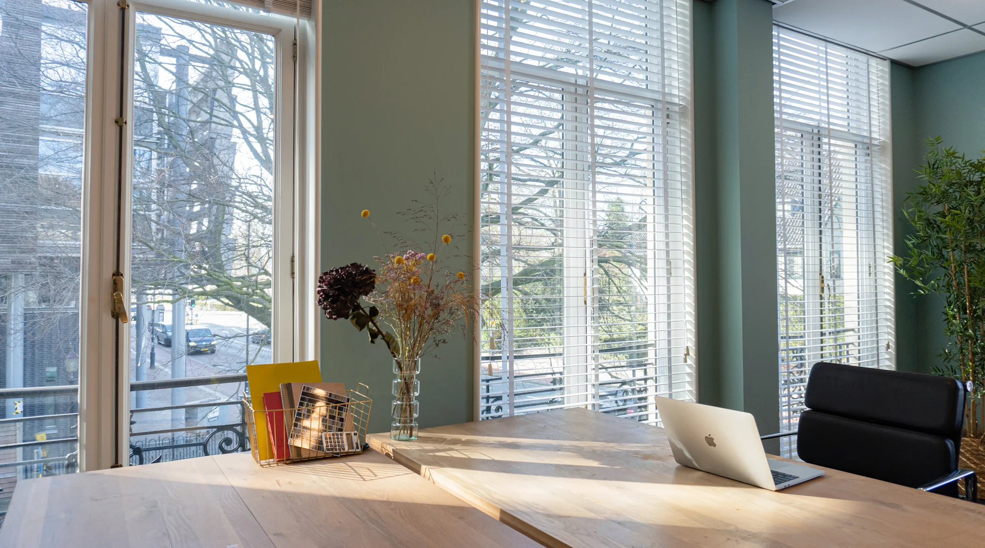 Licht en modern kantoorinterieur in Office Hotel Kennemerplein met houten bureau, laptop en grote ramen met jaloezieën.