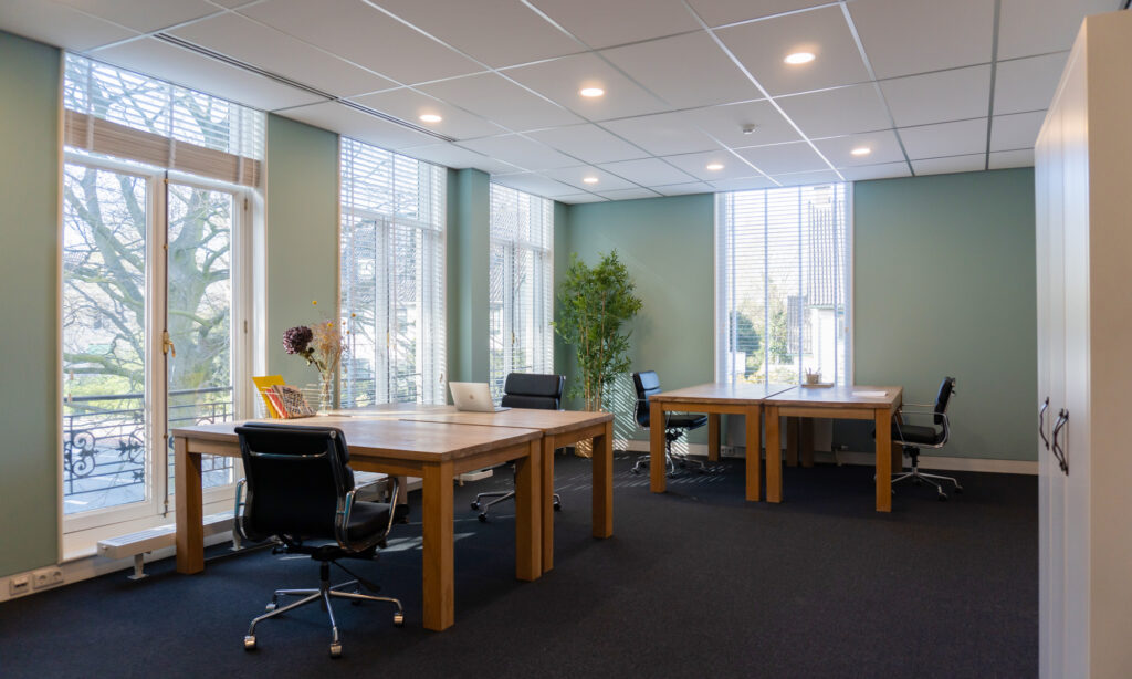 Moderne en lichte kantoorruimte in Office Hotel Kennemerplein met houten bureaus, bureaustoelen en grote ramen.