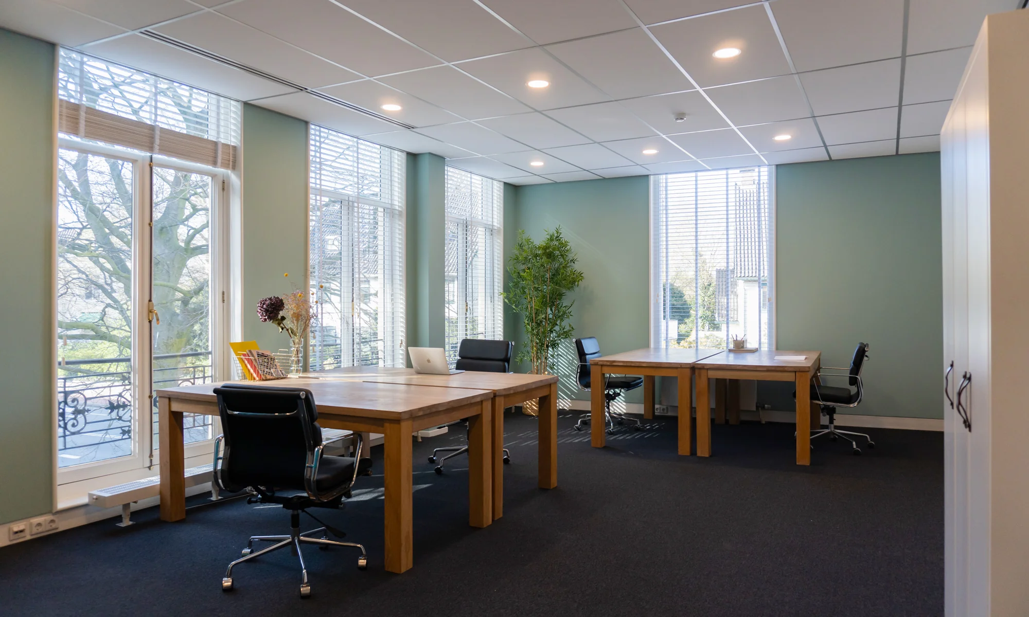 Moderne en lichte kantoorruimte in Office Hotel Kennemerplein met houten bureaus, bureaustoelen en grote ramen.
