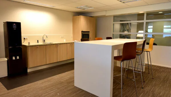 Moderne pantry met houten keukenkastjes, hoge witte tafel en barkrukken in een kantoorruimte aan de Oude Vaartweg 2.