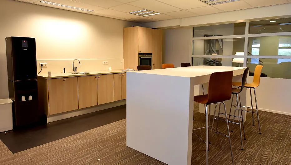 Moderne pantry met houten keukenkastjes, hoge witte tafel en barkrukken in een kantoorruimte aan de Oude Vaartweg 2.