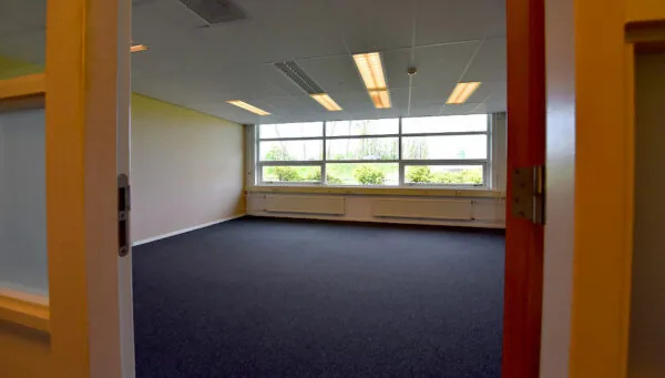 Leeg kantoor met grote ramen en blauw tapijt aan de Oude Vaartweg 2, gezien vanuit een deuropening.