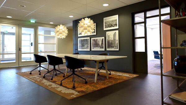 Moderne vergaderruimte aan de Oude Vaartweg 2 met designverlichting, kunst aan de muur en een grote tafel met vijf stoelen.