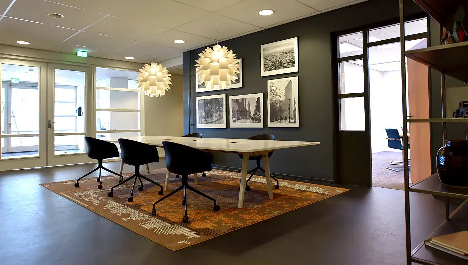 Moderne vergaderruimte aan de Oude Vaartweg 2 met designverlichting, kunst aan de muur en een grote tafel met vijf stoelen.