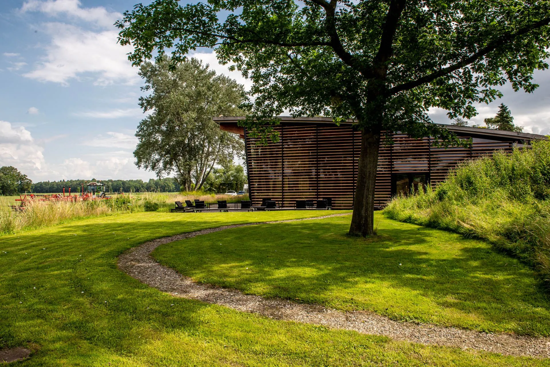 Modern houten gebouw aan de Oudhuizerstraat 31 met een grasveld, bomen en een slingerend pad op de voorgrond.