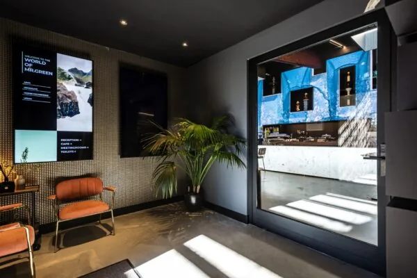 Moderne entree met wachtruimte, een scherm met informatie en doorkijk naar een stijlvol ingerichte koffiebar.