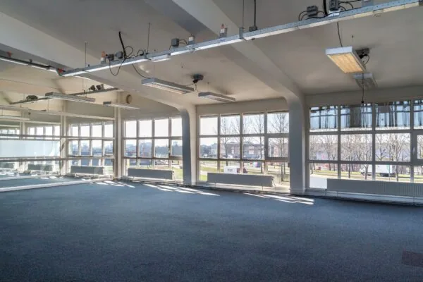 Lichte, leegstaande kantoorruimte aan de Overschieseweg 35 met grote ramen en uitzicht op een bedrijventerrein.