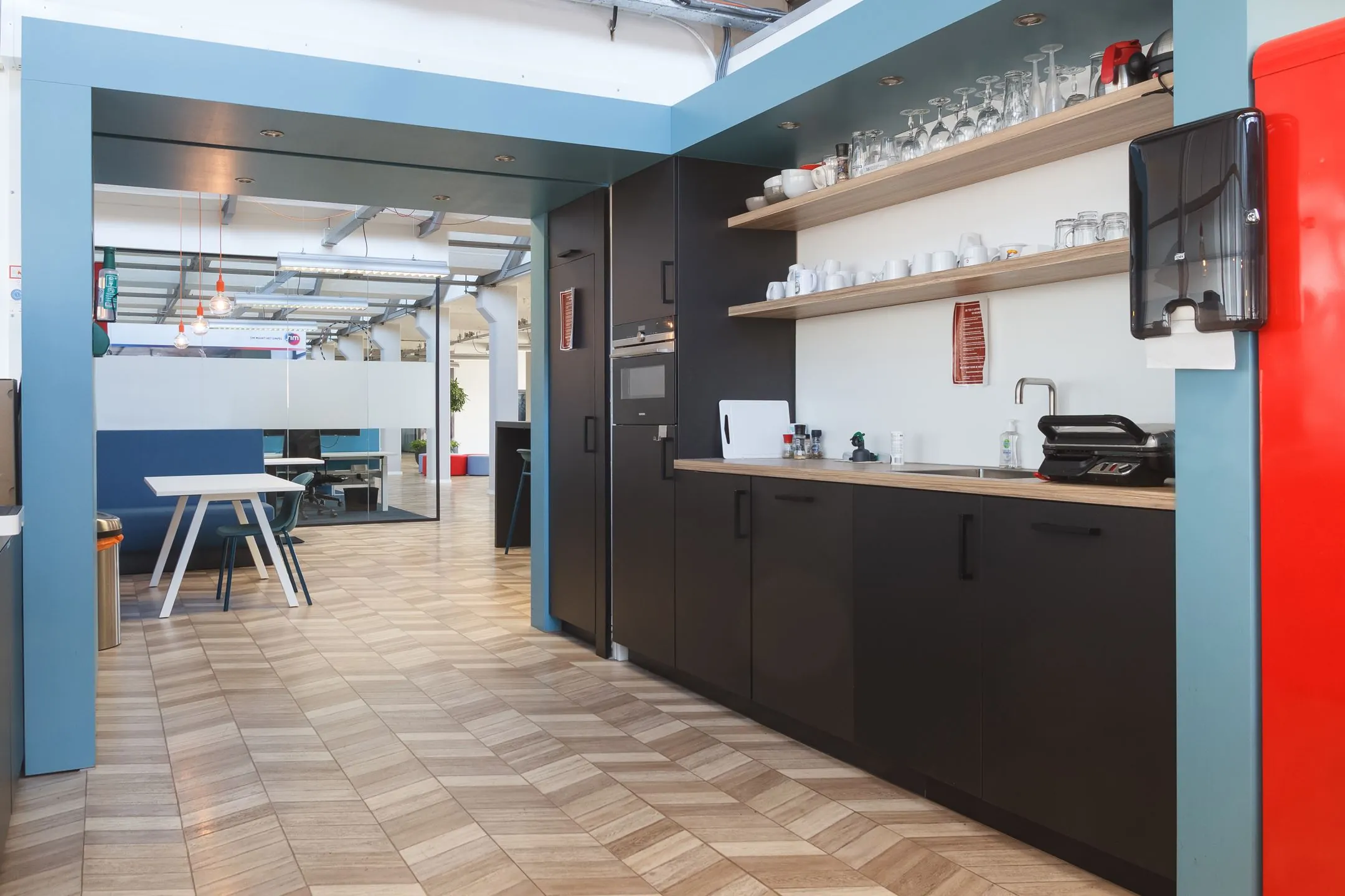 Moderne kantoorkeuken aan de Overschieseweg 35 met zwarte kasten, open houten planken en een zicht op de aangrenzende werkruimte.