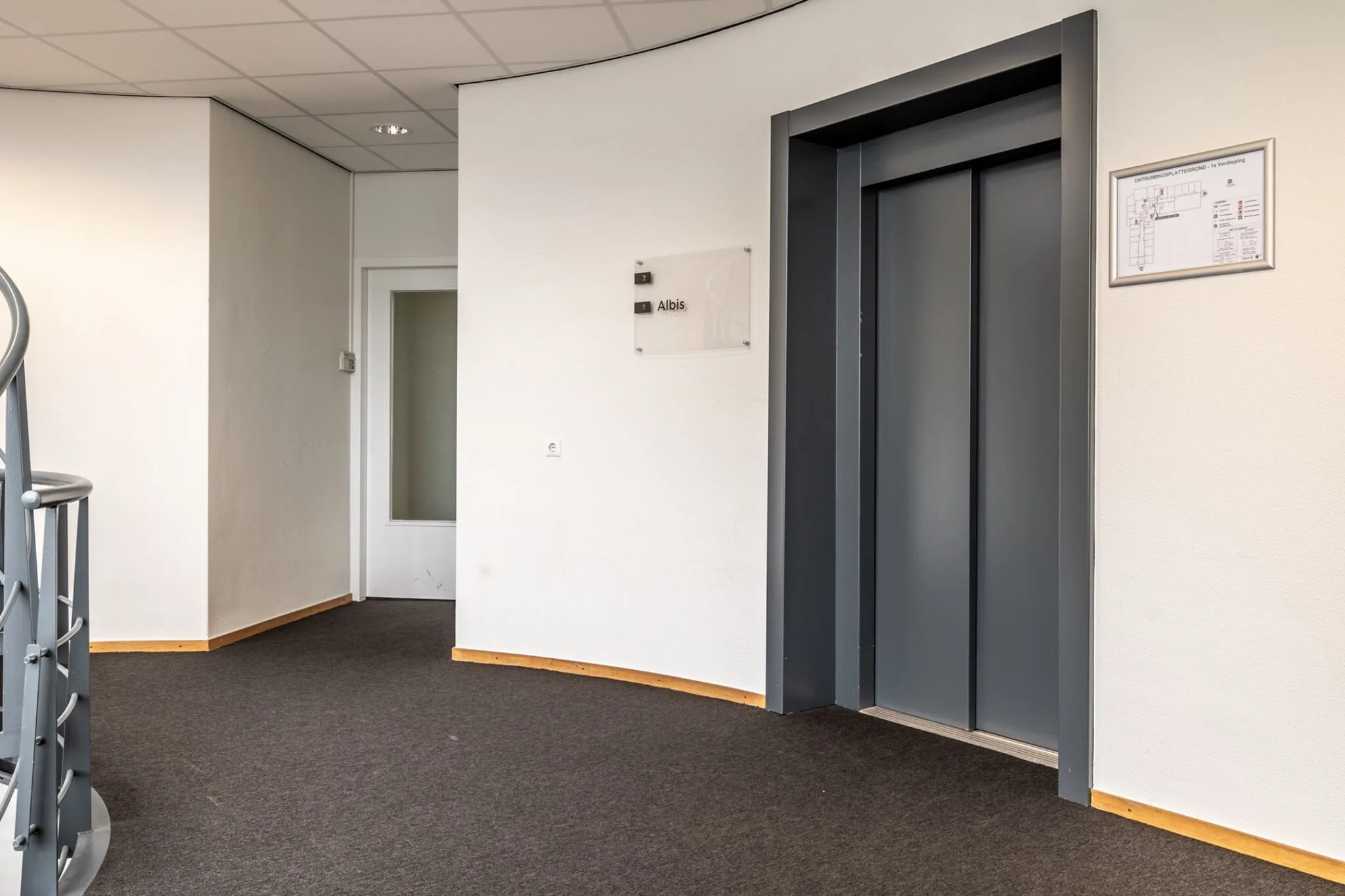 Halfronde gang met grijze liftdeuren, een deur met matglas en een bordje met de naam "Albis".