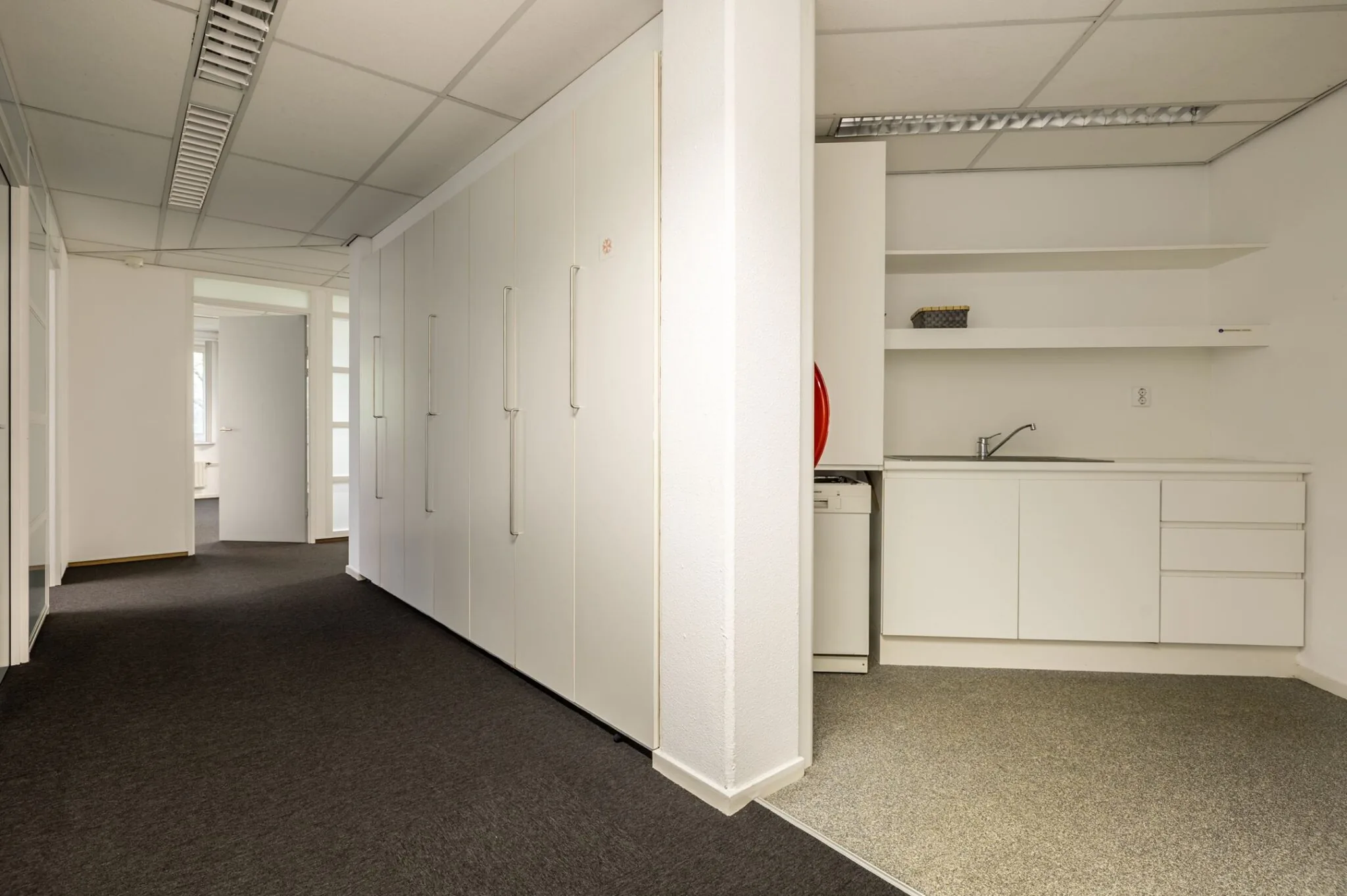 Kantoorruimte met een pantry, witte kastenwand en open deur naar aangrenzende ruimte in Paardeweide 2A-4C.