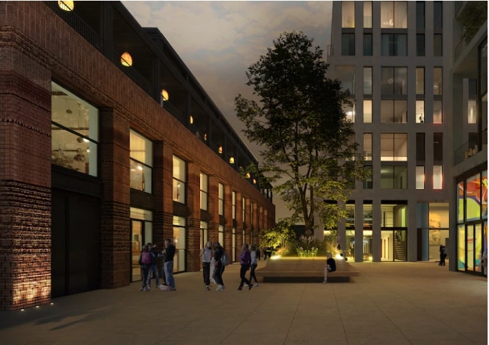 Avondbeeld van Papaverweg 37B met mensen op een modern plein tussen een oud bakstenen pand en een nieuw wit gebouw.