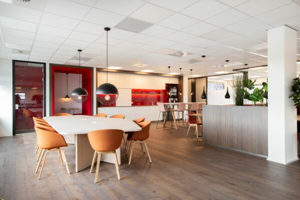 Moderne kantoorruimte aan de Papendorpseweg 75 met open keuken, zithoeken en een grote vergadertafel met oranje stoelen.