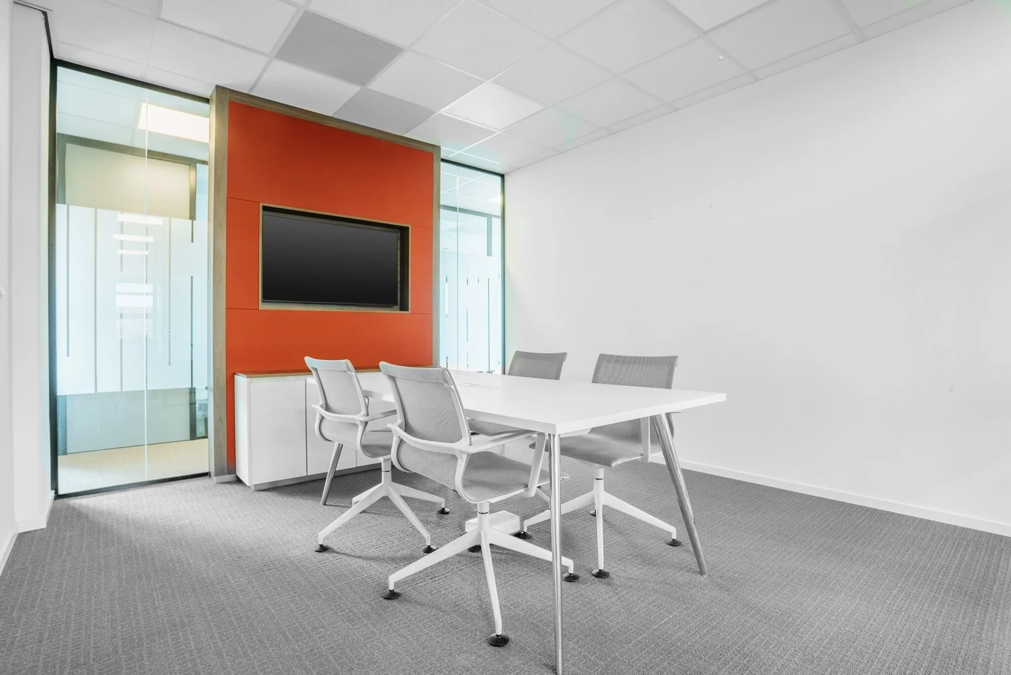 Moderne vergaderruimte aan de Papendorpseweg 75 met witte tafel, grijze stoelen en oranje wand met ingebouwd scherm.