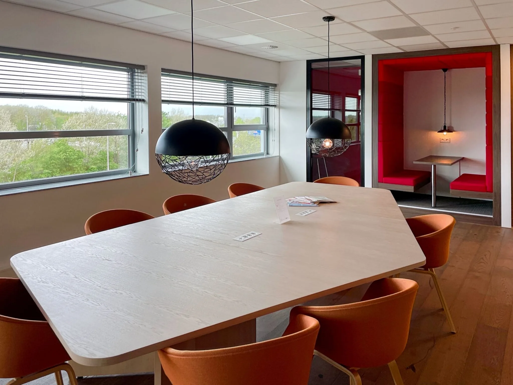 Vergaderruimte aan de Papendorpseweg 75 met grote houten tafel, oranje stoelen, moderne verlichting en rode zitnis.