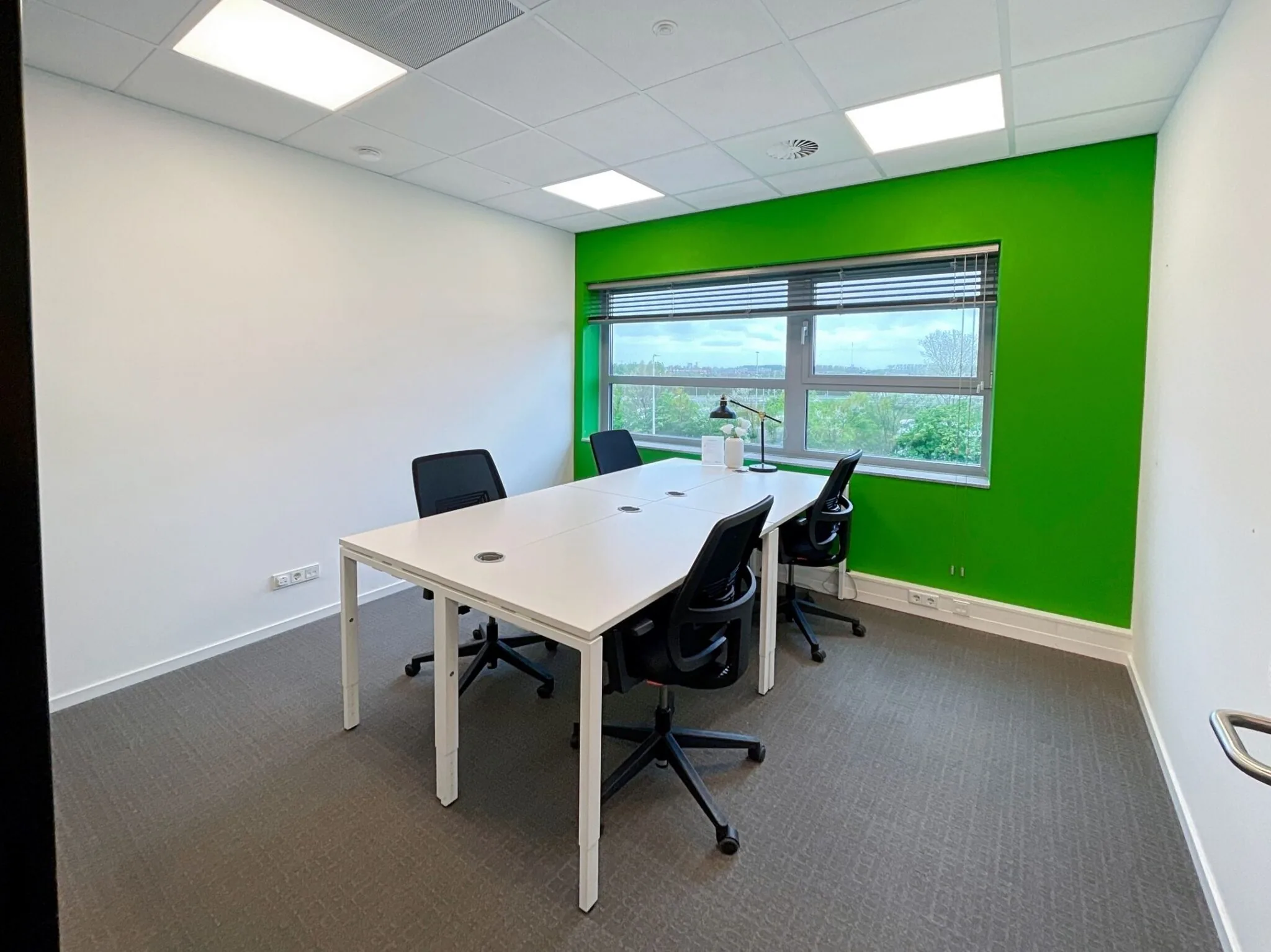 Kleine vergaderruimte aan de Papendorpseweg 75 met vier bureaustoelen, witte tafels en een heldergroene accentmuur.