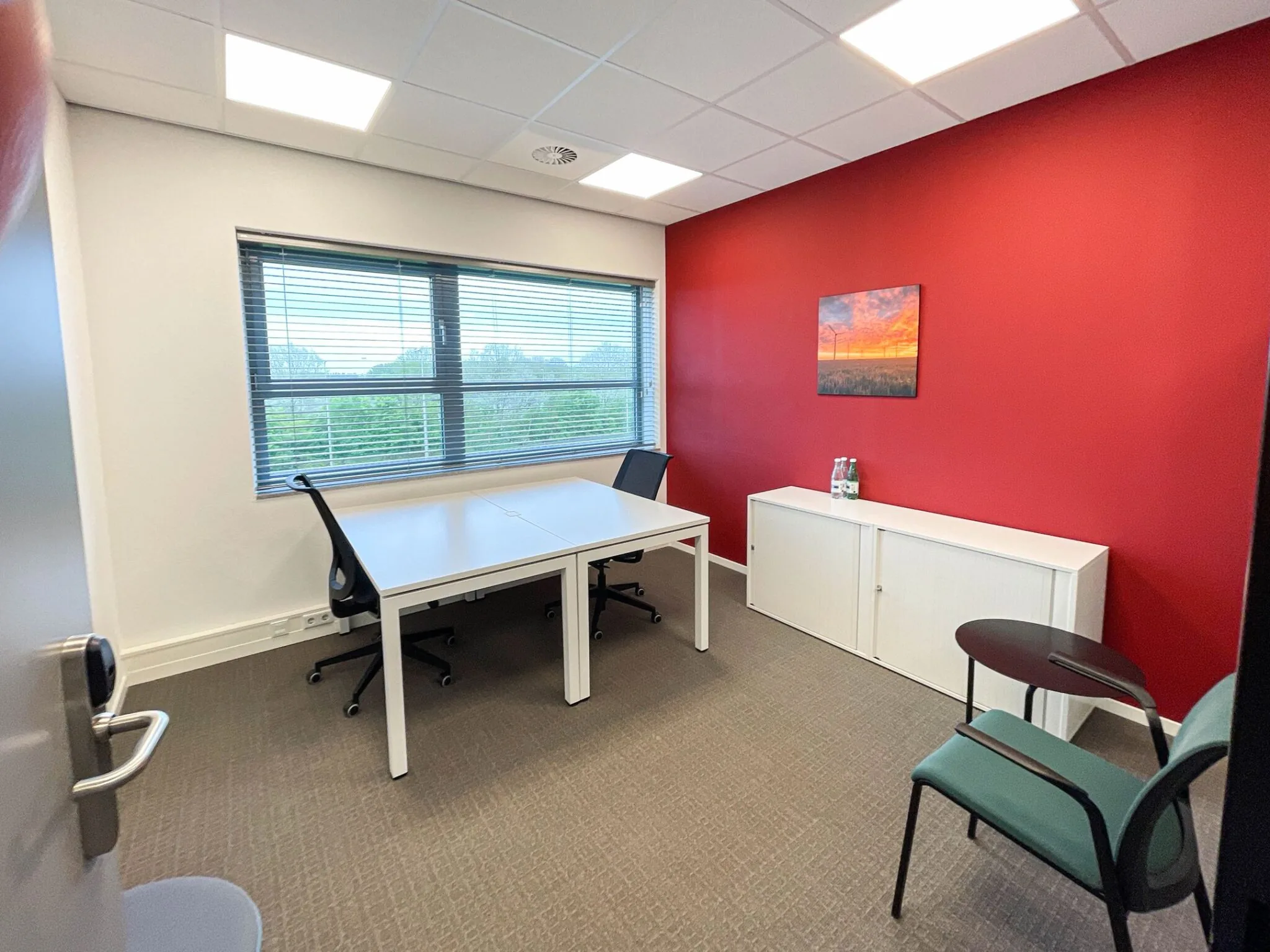 Kleine kantoorruimte aan de Papendorpseweg 75 met twee bureaus, een rood accentmuur en uitzicht op groen.