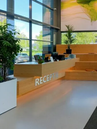Moderne receptiebalie van hout met planten en grote ramen aan de Papendorpseweg 75.