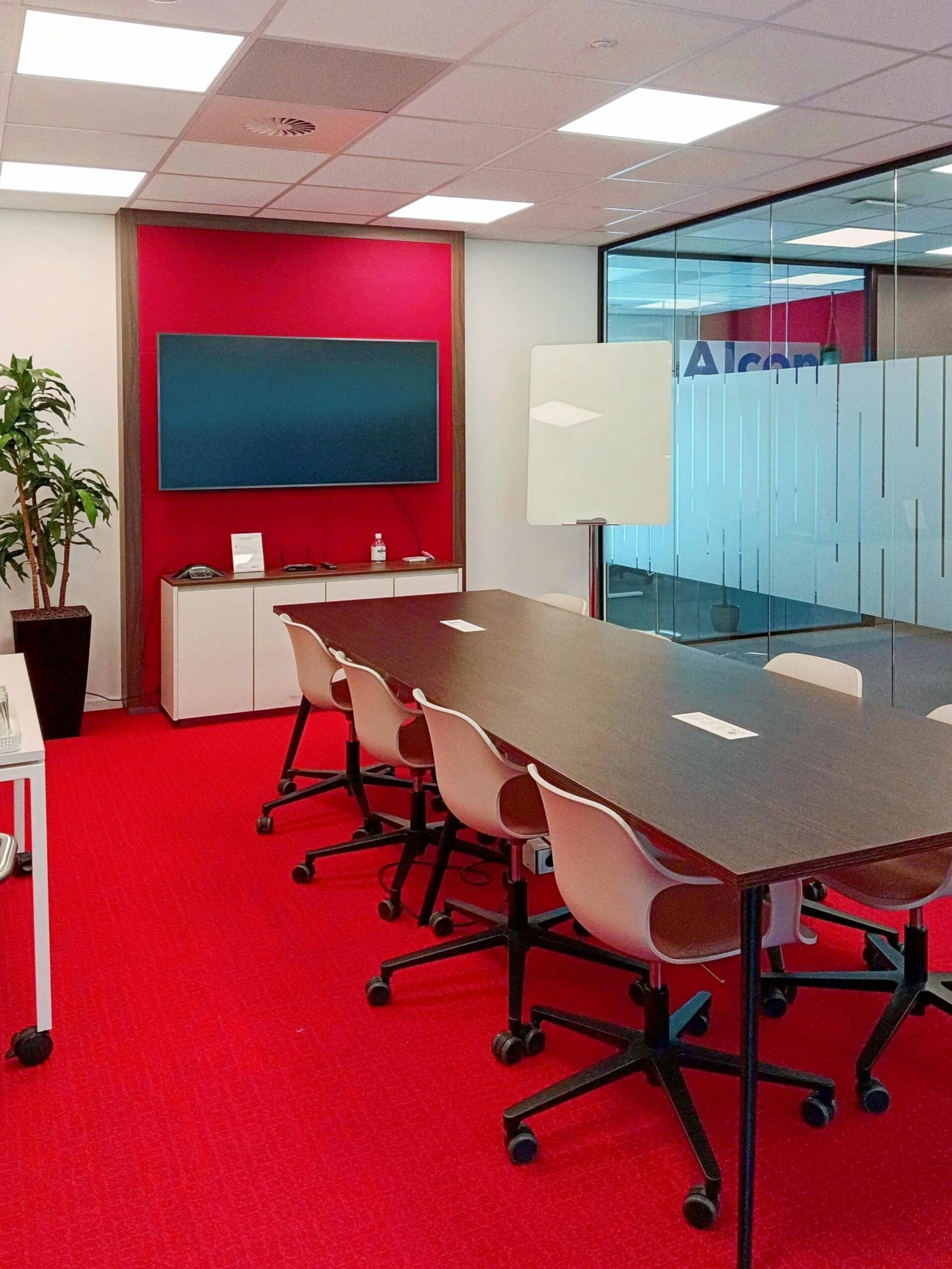 Vergaderruimte met rode vloerbedekking, een lange tafel met stoelen, een groot scherm en een glazen wand bij Papendorpseweg 75.