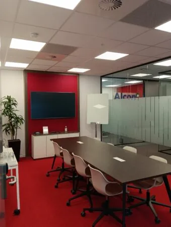 Vergaderruimte aan de Papendorpseweg 75 met rode vloerbedekking, een lange tafel, stoelen, een flatscreen en glazen wanden.