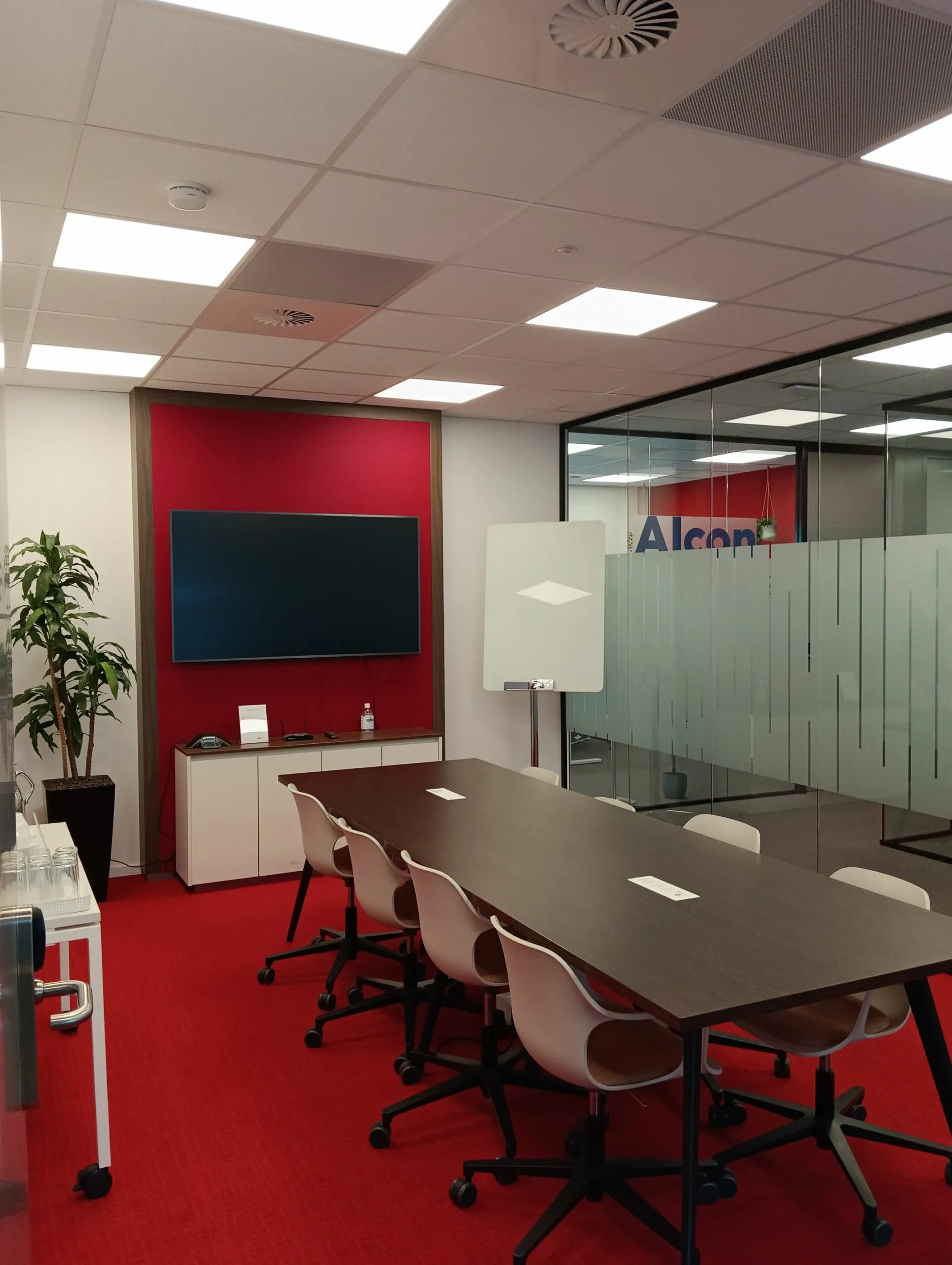 Vergaderruimte aan de Papendorpseweg 75 met rode vloerbedekking, een lange tafel, stoelen, een flatscreen en glazen wanden.