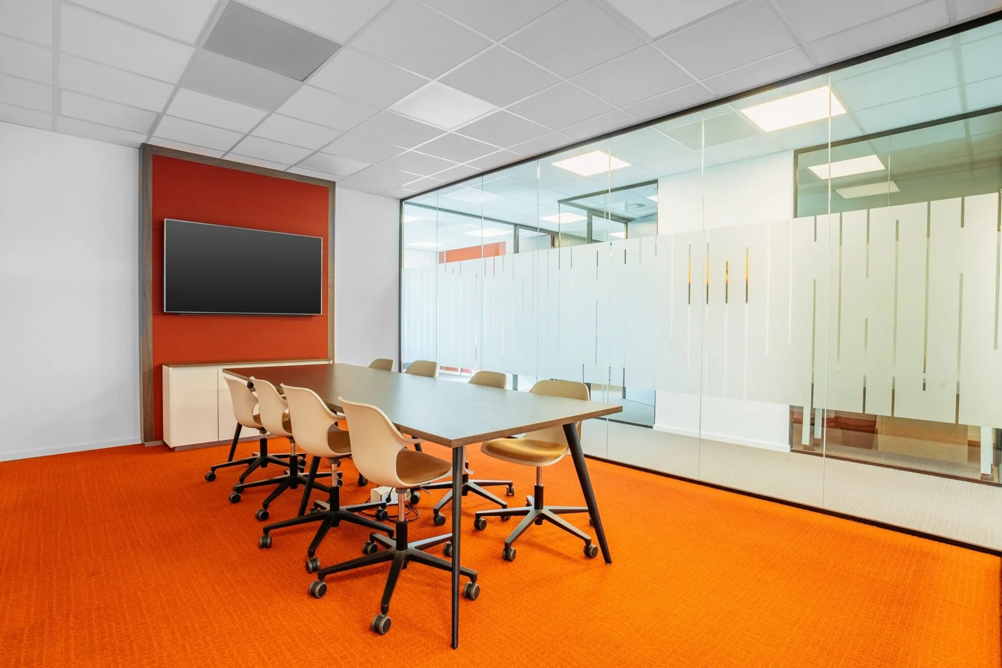 Vergaderruimte aan de Papendorpseweg 75 met oranje vloerbedekking, glazen wand en groot presentatiescherm.