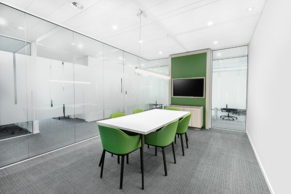 Moderne vergaderruimte aan de Papendorpseweg 95 met groene stoelen, een witte tafel, glazen wanden en een flatscreen aan de muur.
