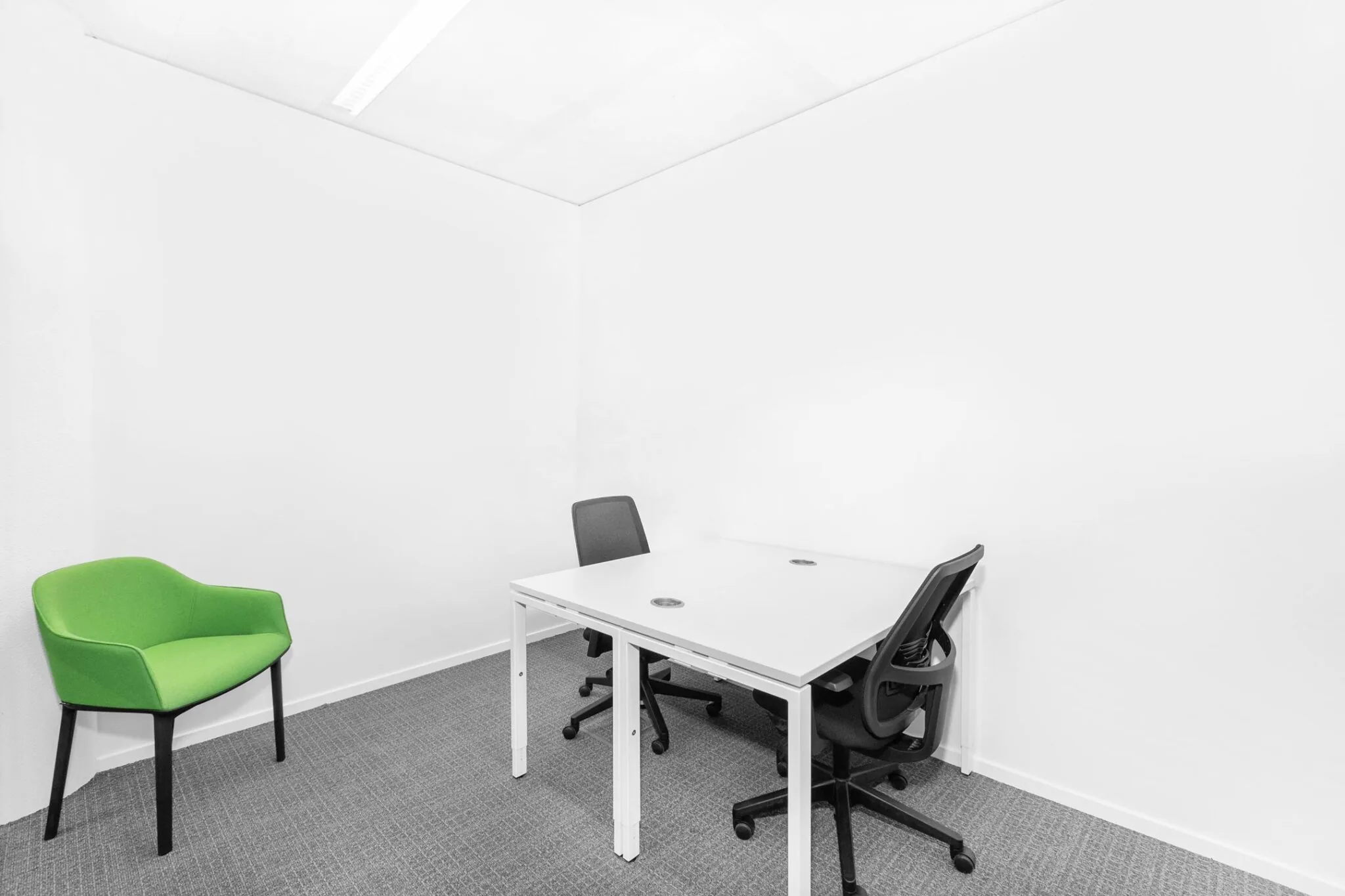 Kleine, witte kantoorruimte met twee bureaustoelen, een wit bureau en een groene fauteuil.