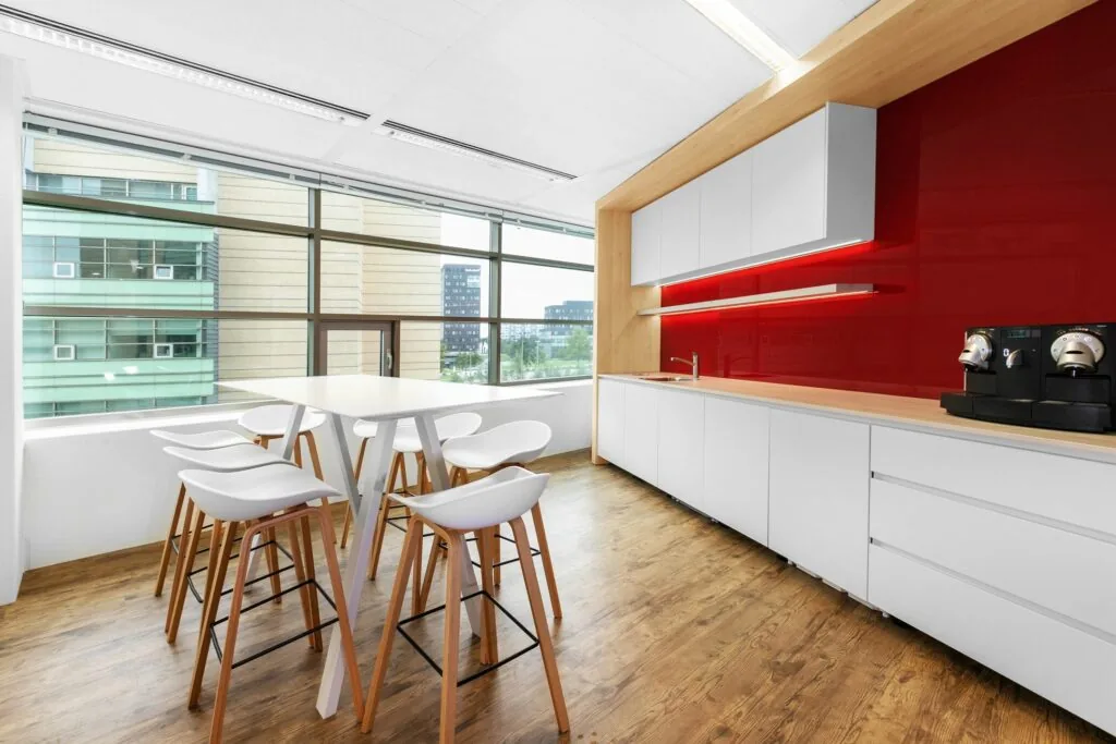Moderne kantoorkeuken aan de Papendorpseweg 95 met witte kasten, rode achterwand, koffiemachines en hoge zitplaatsen bij een bartafel.